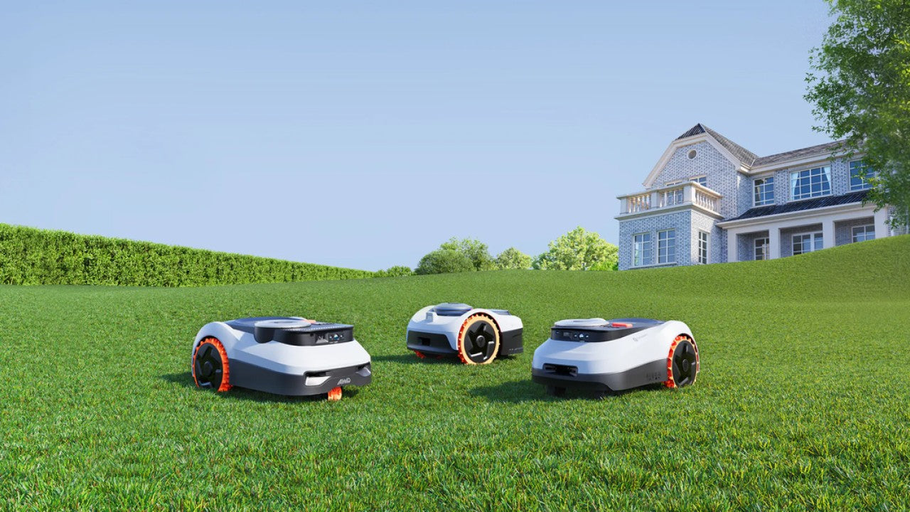 Drie robotmaaiers op een groen gazon voor een huis, met oranje accenten op de wielen en een moderne, compacte vormgeving.